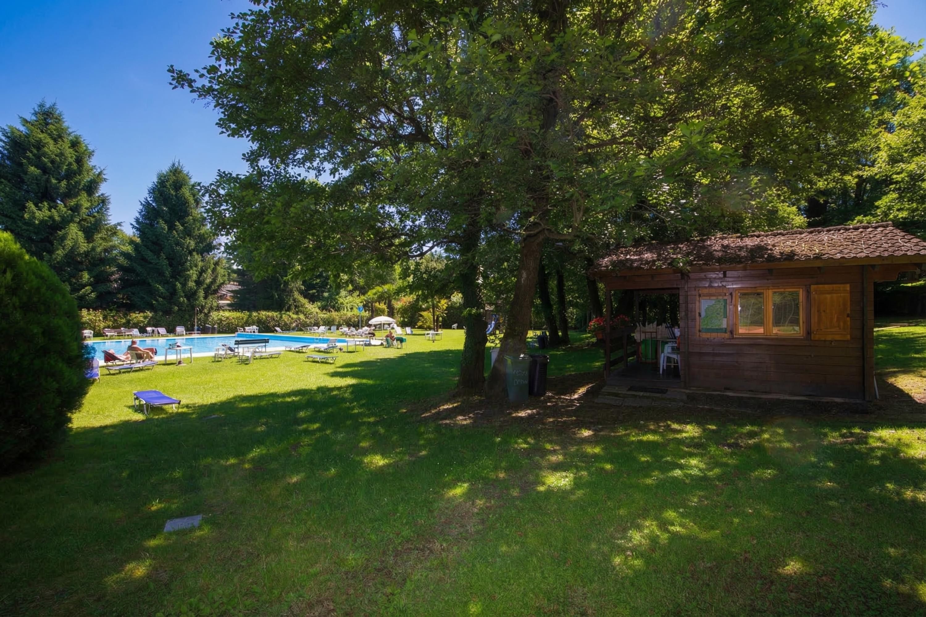 Una cabaña de madera con techo de tejas, rodeada de césped, piscina y sillas de descanso.