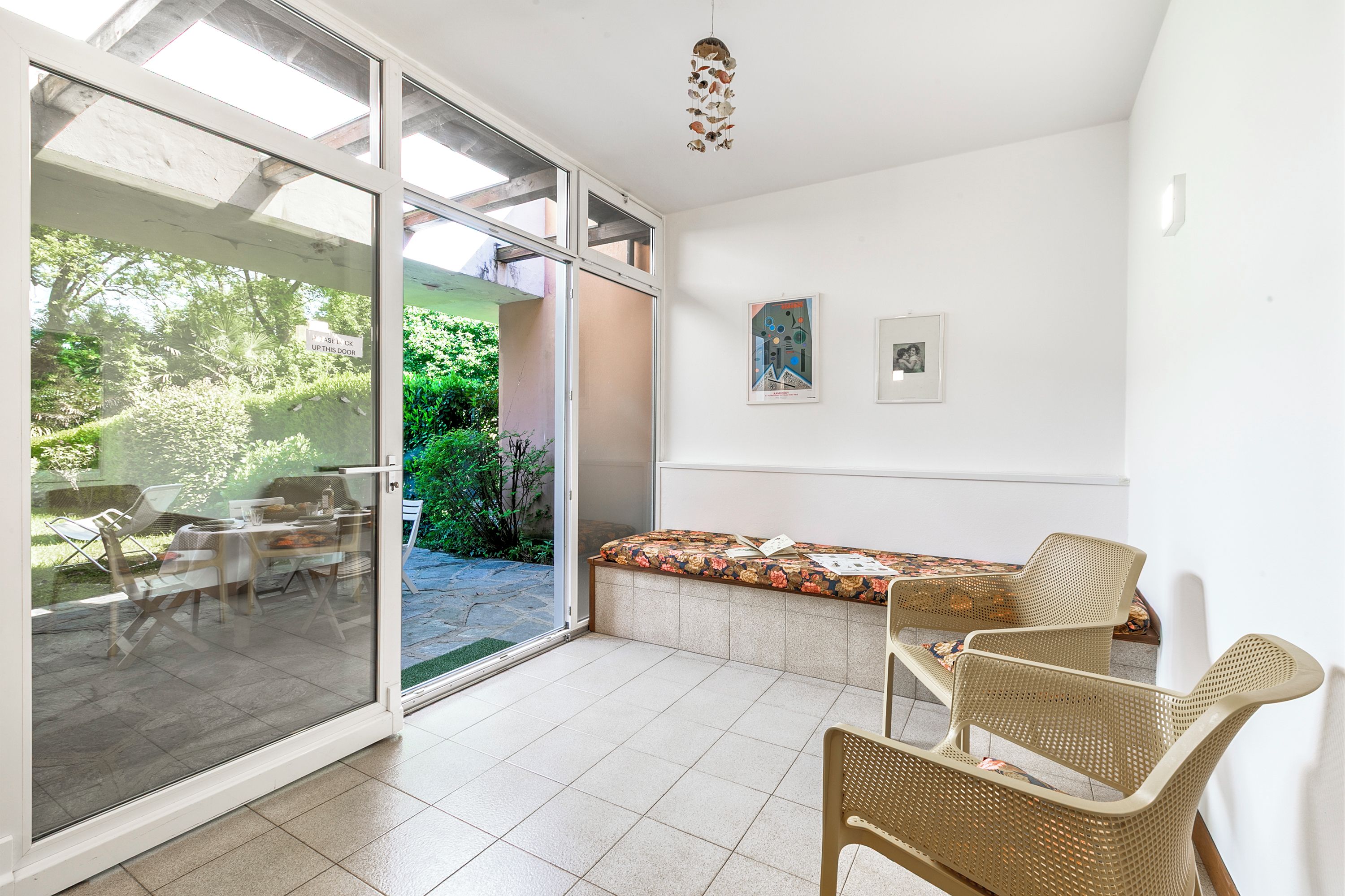 Una habitación con puerta corrediza de vidrio que da a un patio, un banco acolchado y sillas de mimbre.