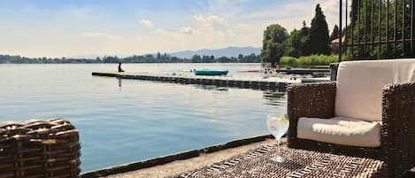 Eine friedliche Seebucht mit Korbmöbeln und einem Glas Wein, mit Blick auf ruhiges Wasser und ferne Berge.