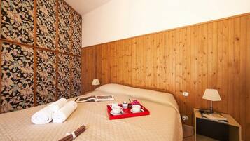 A hotel room with a wooden headboard, a bed with a quilted bedspread, a bedside table with a lamp, and a tray with towels and a book.