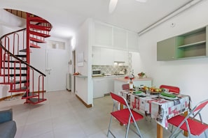 Una cucina compatta con mobili bianchi, un forno a microonde e un'area pranzo con un tavolo apparecchiato per due.