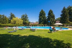A swimming pool surrounded by grass, trees, and a building in the background.