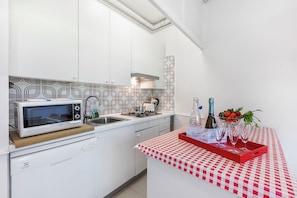 A compact kitchen with white cabinets, a microwave, a gas stove, and a red checkered tablecloth.