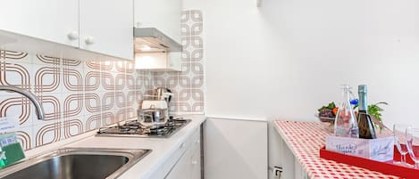 Et kompakt køkken med hvide skabe, en stålvask, en gasblus og mønstrede backsplash-fliser.
