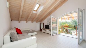 Un salon moderne doté d’un plafond en pente, d’un canapé, d’un meuble pour la télévision et d’une porte-fenêtre coulissante donnant sur un balcon extérieur.