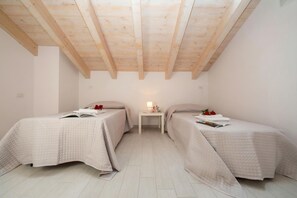 A room with two beds, a small table with a lamp, and a sloped ceiling with wooden beams. - Silver Lake Apartment (Angera)