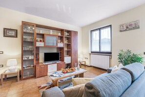 Uma sala de estar com sofá, mesa de centro com revistas, televisão e aparador de madeira com portas de vidro.