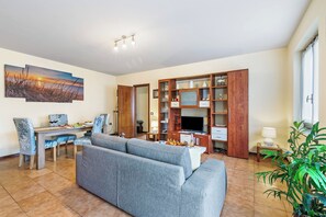 A living room with a sofa, dining table, and chairs. There is a TV, wooden cabinets, and a plant.