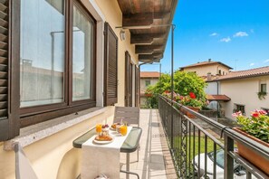 A balcony with a table set for breakfast, a railing, and a view of the neighborhood.