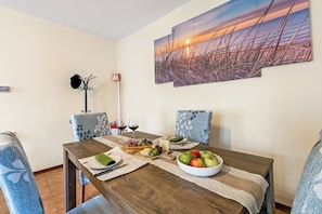 A dining area with a wooden table, chairs, a painting of a sunset, and a fire extinguisher. - Sunrise in Baveno (Baveno)