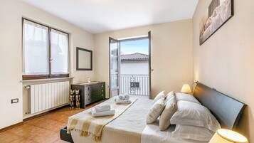 Une chambre à coucher avec un lit, des lampes de chevet, une commode, un radiateur et une vue sur le balcon.