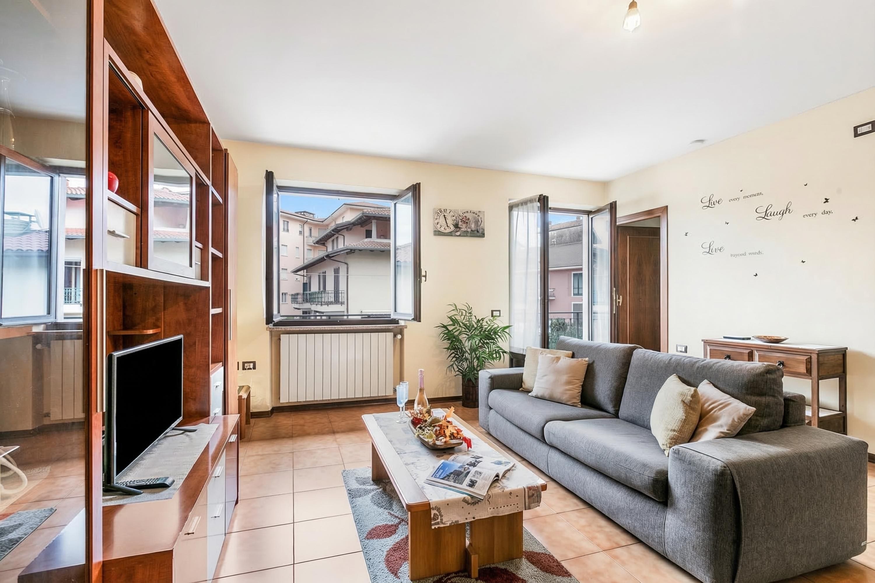 A living room with a sofa, coffee table, TV, and open windows.