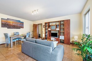 A living room with a sofa, dining table, chairs, TV, wooden cabinet, and a painting on the wall.