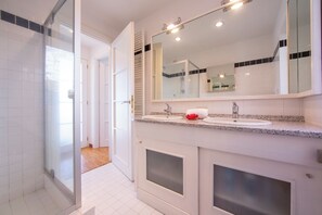 Un baño moderno con cabina de ducha de vidrio, tocador doble y un espejo grande.
