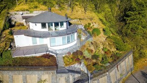 Een modern huis met een gebogen dak, grote ramen en een stenen keerwand.