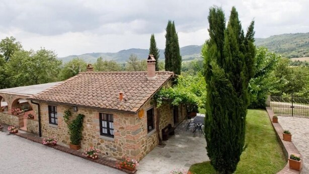 A stone house with a tiled roof, surrounded by a well-maintained lawn and tall trees. - Agriturismo Incrociata (Bucine)