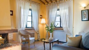 A cozy living room with a fireplace, wicker chair, sofa, and a table with a vase of flowers. - Agriturismo Incrociata (Bucine)