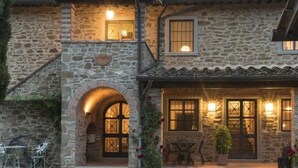 A stone building with a central arched entrance, a balcony with seating, and a small garden area. - Agriturismo Incrociata (Bucine)