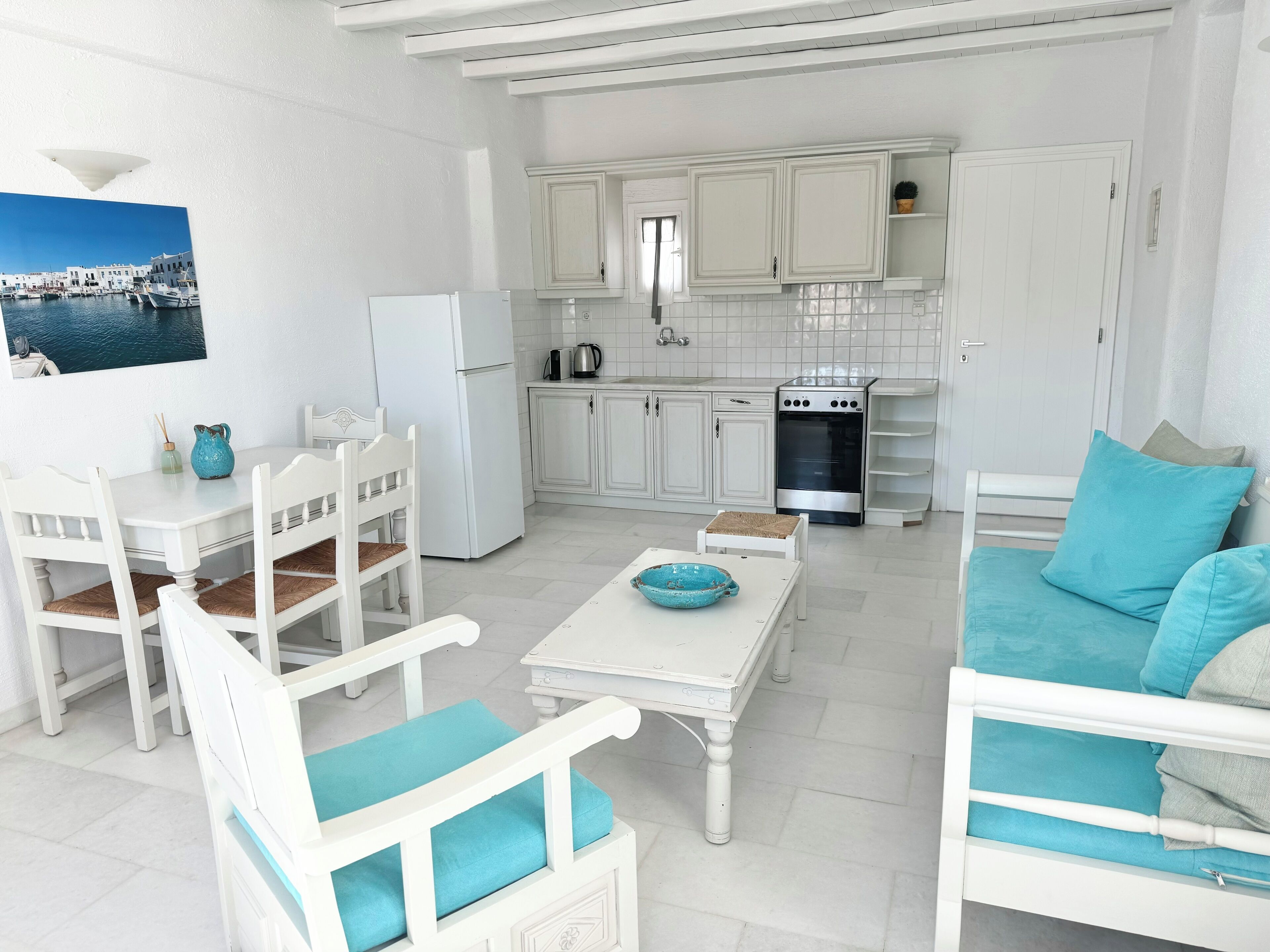 Un soggiorno in tonalità bianco con angolo da pranzo, cucina e vista sul mare.