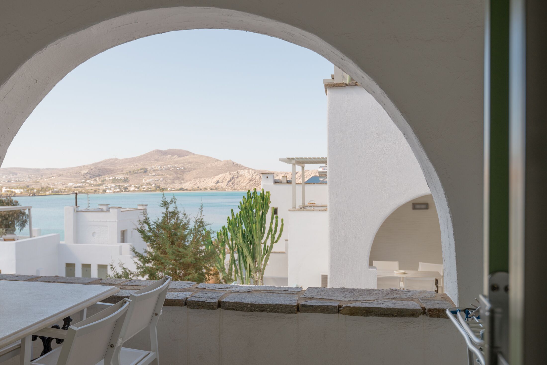 A balcony with a view of a coastal landscape, including a body of water and distant hills.
