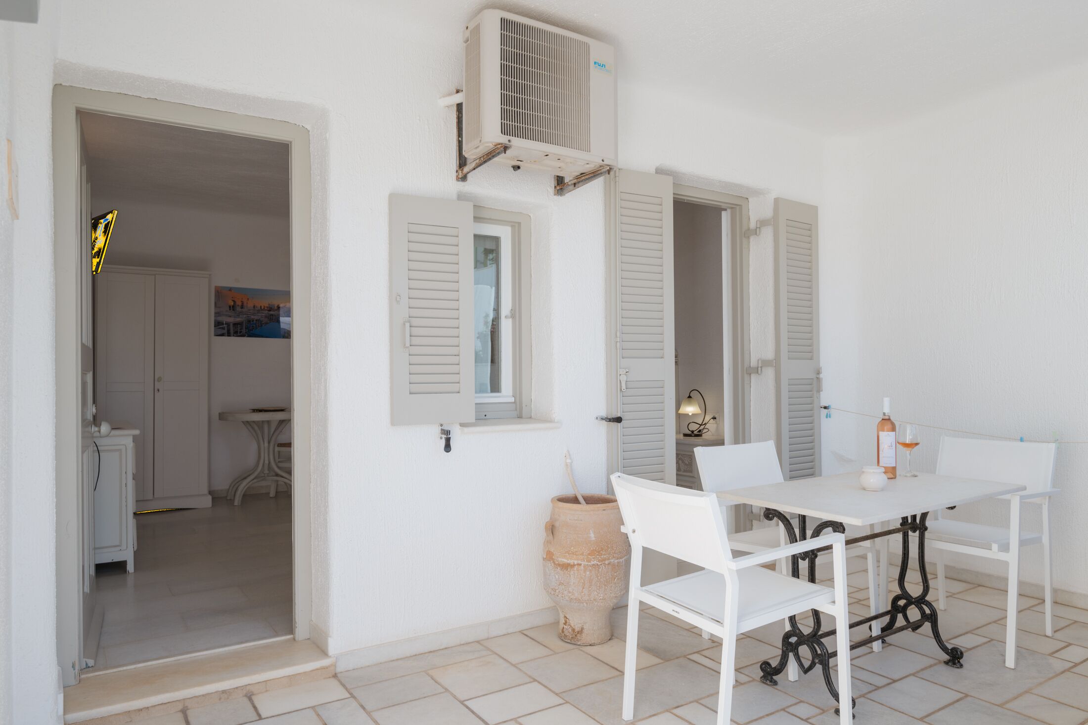 A white room with a table and chairs, a window with shutters, and an air conditioning unit.