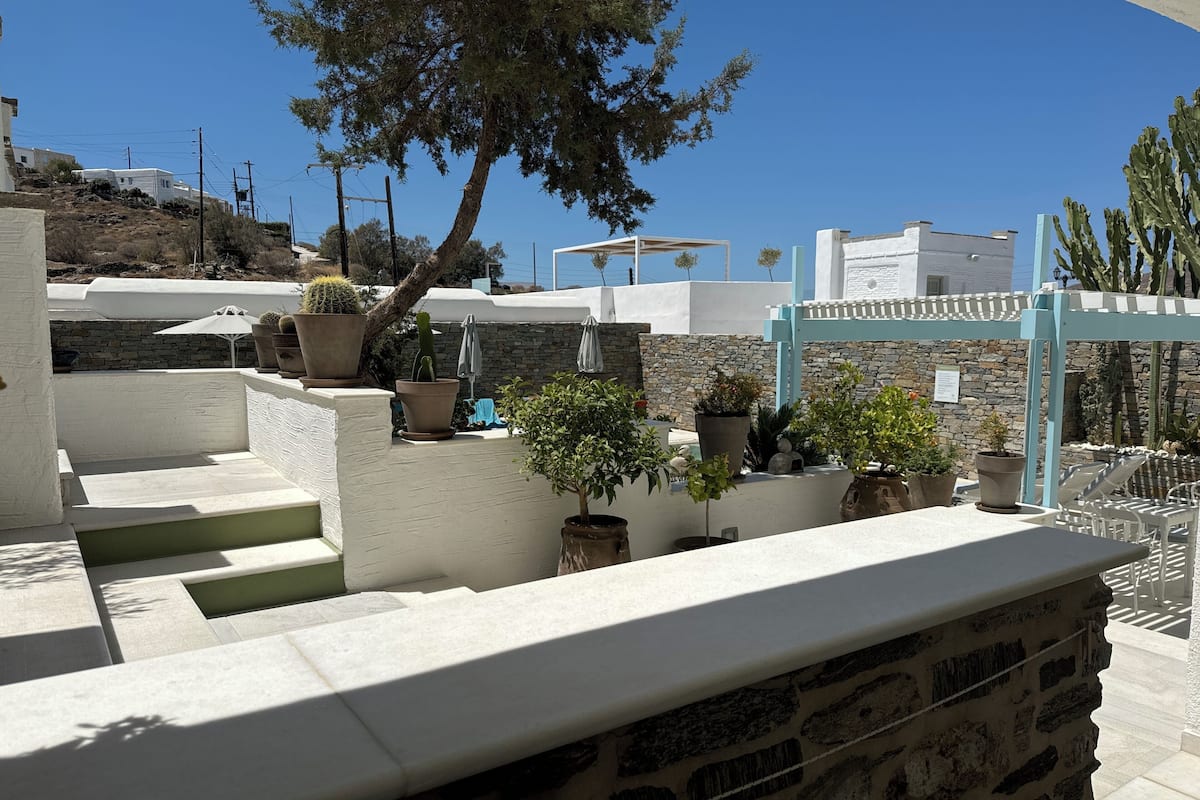 A white-walled outdoor area with a stone staircase, potted plants, and a view of the sea.