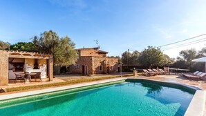 A swimming pool with lounge chairs, a barbecue area, and a stone building with a tiled roof. - A rural idyll with pool – Villa Es Figueral (Campos)