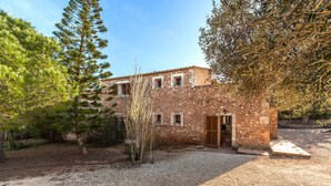 A stone building with a door and windows, surrounded by trees and gravel. - A rural idyll with pool – Villa Es Figueral (Campos)