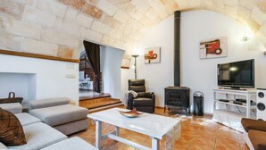 A living room with a fireplace, sofa, television, and a stone archway. - A rural idyll with pool – Villa Es Figueral (Campos)