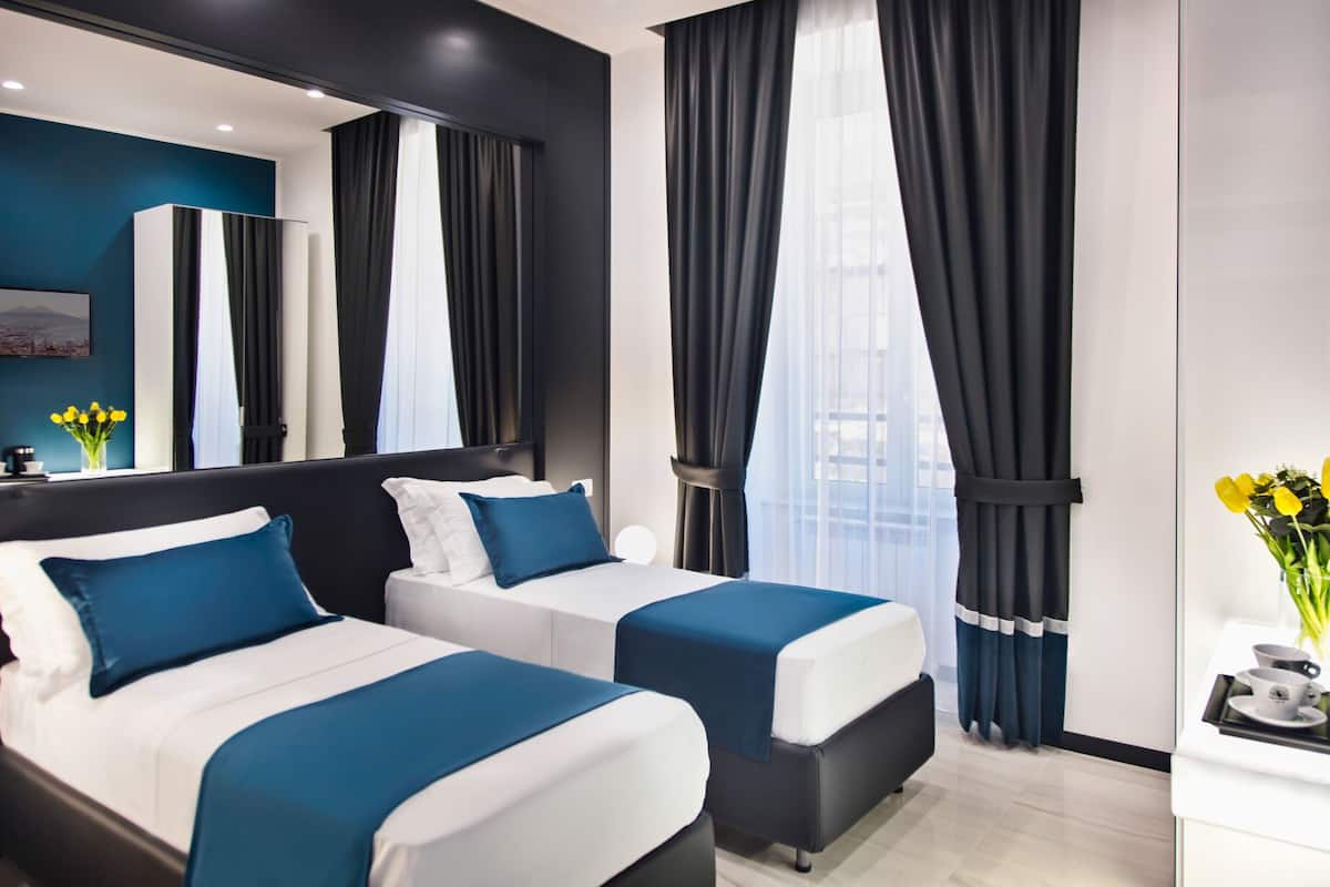 A modern hotel room with two beds, a large mirror, and a view of the city.