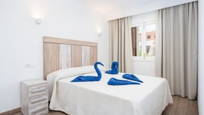 A hotel room with a bed, a nightstand, a window with curtains, and a view of buildings outside. - Beautiful Apartment "Venecia" with Pool, Wi-Fi, Balcony & A/C (Alcudia)