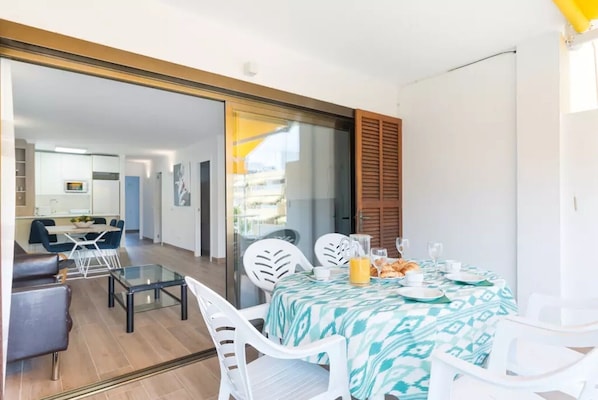 A dining area with a table set for two, a kitchen in the background, and a sliding glass door leading to an outdoor area.