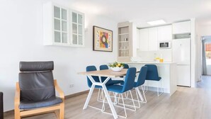 A modern kitchen with white cabinets, a dining area with blue chairs, and a grey leather chair. - Beautiful Apartment "Venecia" with Pool, Wi-Fi, Balcony & A/C (Alcudia)