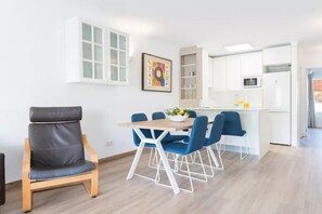 A modern kitchen with white cabinets, a dining area with blue chairs, and a grey leather chair.