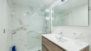 A modern bathroom with a glass shower enclosure, a white sink, and a wooden vanity. - Beautiful Apartment "Venecia" with Pool, Wi-Fi, Balcony & A/C (Alcudia)