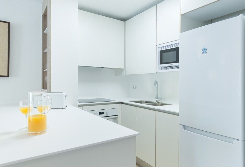 Une cuisine moderne avec des meubles blancs, un four à micro-ondes, un réfrigérateur et un grille-pain.