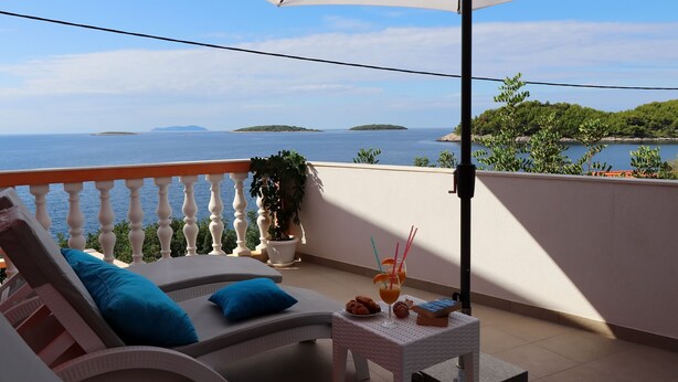 A balcony with a view of the sea, a lounge chair, a small table with drinks, and a potted plant. - Holiday Home Adriatic View (Blato)