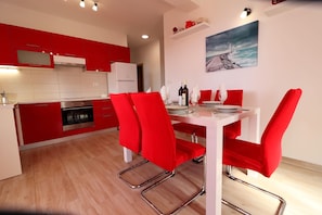 A modern kitchen with red cabinets, a white dining table, and red chairs.