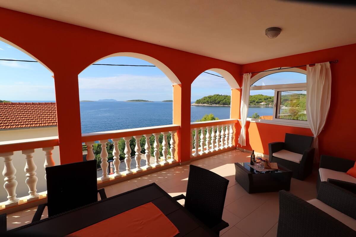 A balcony with a view of the sea and a distant island, furnished with black and white chairs and a table.