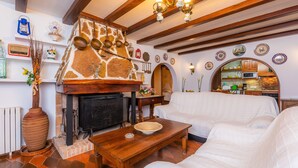 Een gezellige woonkamer met een open haard, een witte bank, een houten salontafel, en een keuken zichtbaar door een boogvormige deuropening.