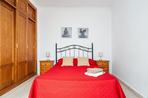 Un dormitorio con cama, armario de madera, dos mesitas de noche y dos cuadros colgados en la pared.