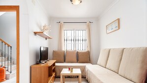 A cozy living room with a sofa, a TV, a small table, and a window with curtains. - Charming Apartment in Great Location Near the Beach with Terrace; Pets Allowed under request (Conil de la Frontera)