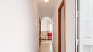 A hallway with a bed, a red sofa, and a door with a glass panel. - Charming Apartment in Great Location Near the Beach with Terrace; Pets Allowed under request (Conil de la Frontera)
