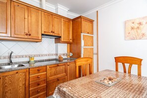 Una cocina con armarios de madera, un lavamanos de acero inoxidable y una mesa de comedor con mantel tejido.