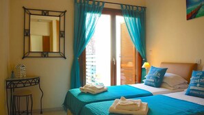 A hotel room with two beds, a small table with a chair, a mirror, and a window with curtains. - Villa HG30 - Destu (Kouklia)