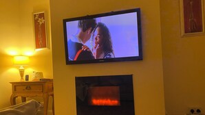 Un salon avec un téléviseur fixé au mur, une cheminée en dessous, une lampe sur une table d’appoint et un canapé.