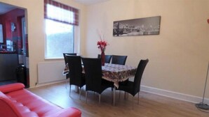 Un coin repas avec une table dressée pour quatre personnes, entouré de chaises noires, d’un canapé rouge et d’une fenêtre avec des stores.