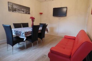 A dining area with a table set for four, a red sofa, a flat-screen TV mounted on the wall, and a framed picture above the table. - SOUTH LAKES TOWN HOUSE (Barrow-in-Furness)