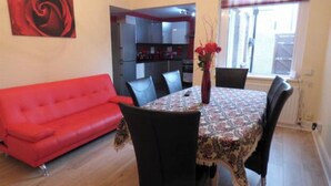 Un coin repas avec une table dressée pour quatre personnes, un canapé rouge et une cuisine en arrière-plan.