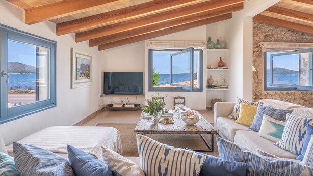 A spacious living area with a high wooden ceiling, a sofa set, a coffee table with decorative items, and a television. - Stone villa on the sea – Villa Can Cuarassa (Pollença)
